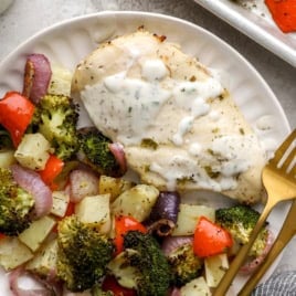 A plate of baked Ranch chicken and veggies topped with extra Ranch.