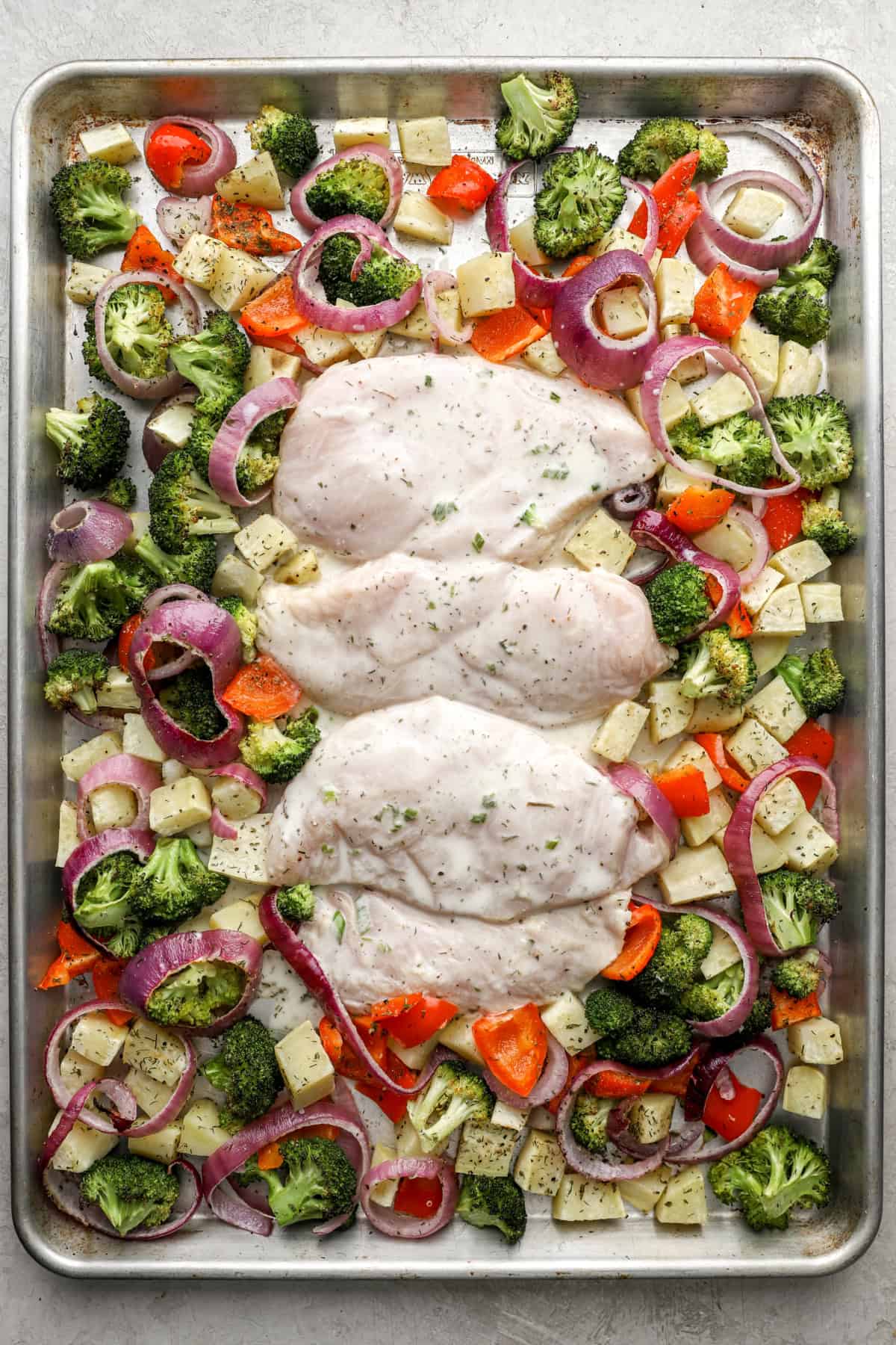 Raw Ranch chicken on a baking sheet with veggies. 