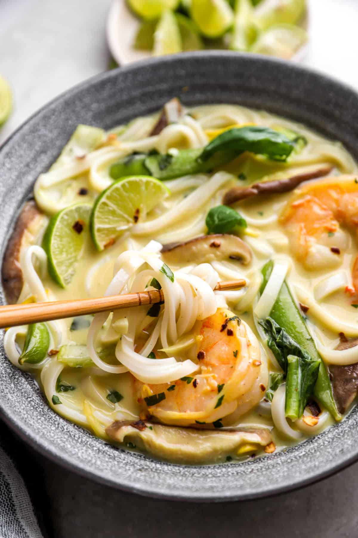 Chopsticks lifting noodles from a pot of Thai curry soup. 