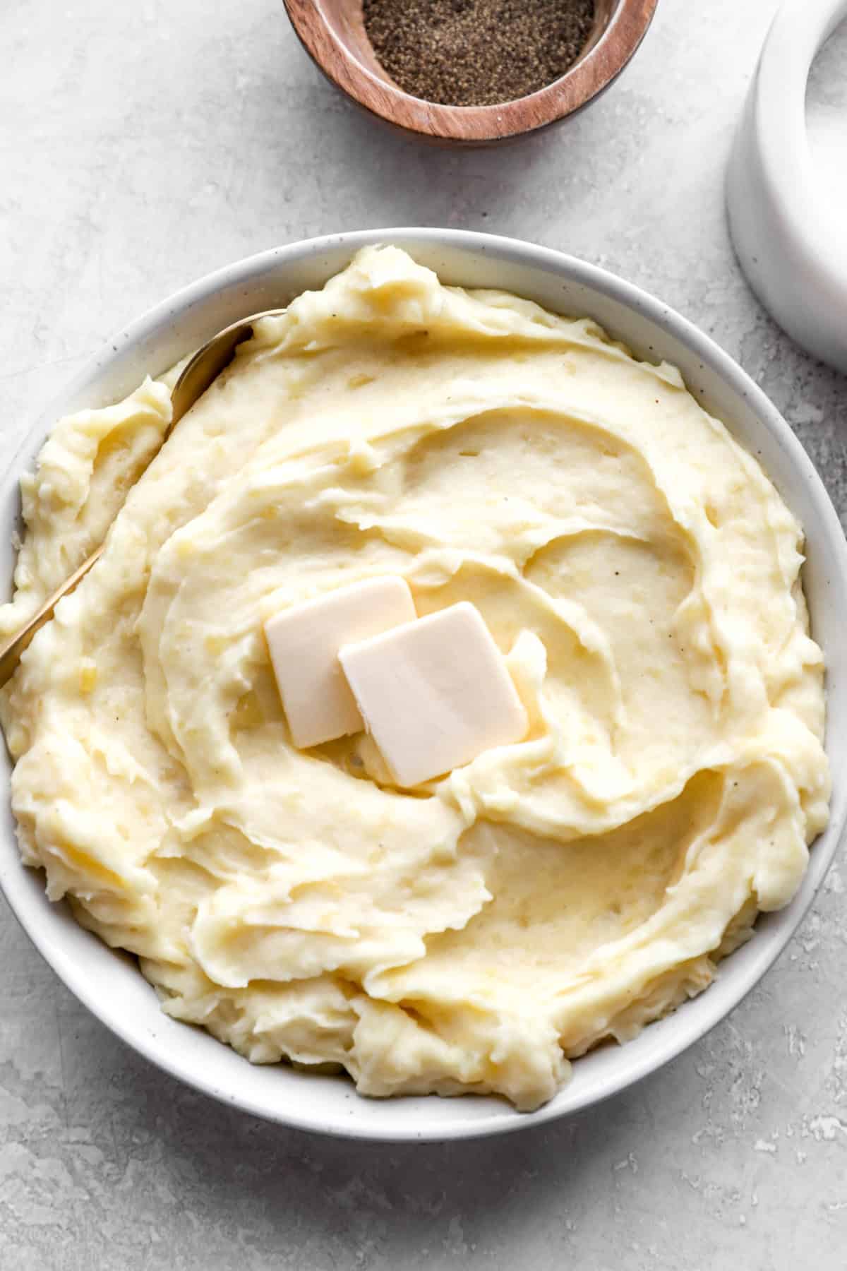 A bowl of mashed potatoes topped with two pads of butter. 