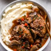 A bowl of chicken coq au vin over mashed potatoes.