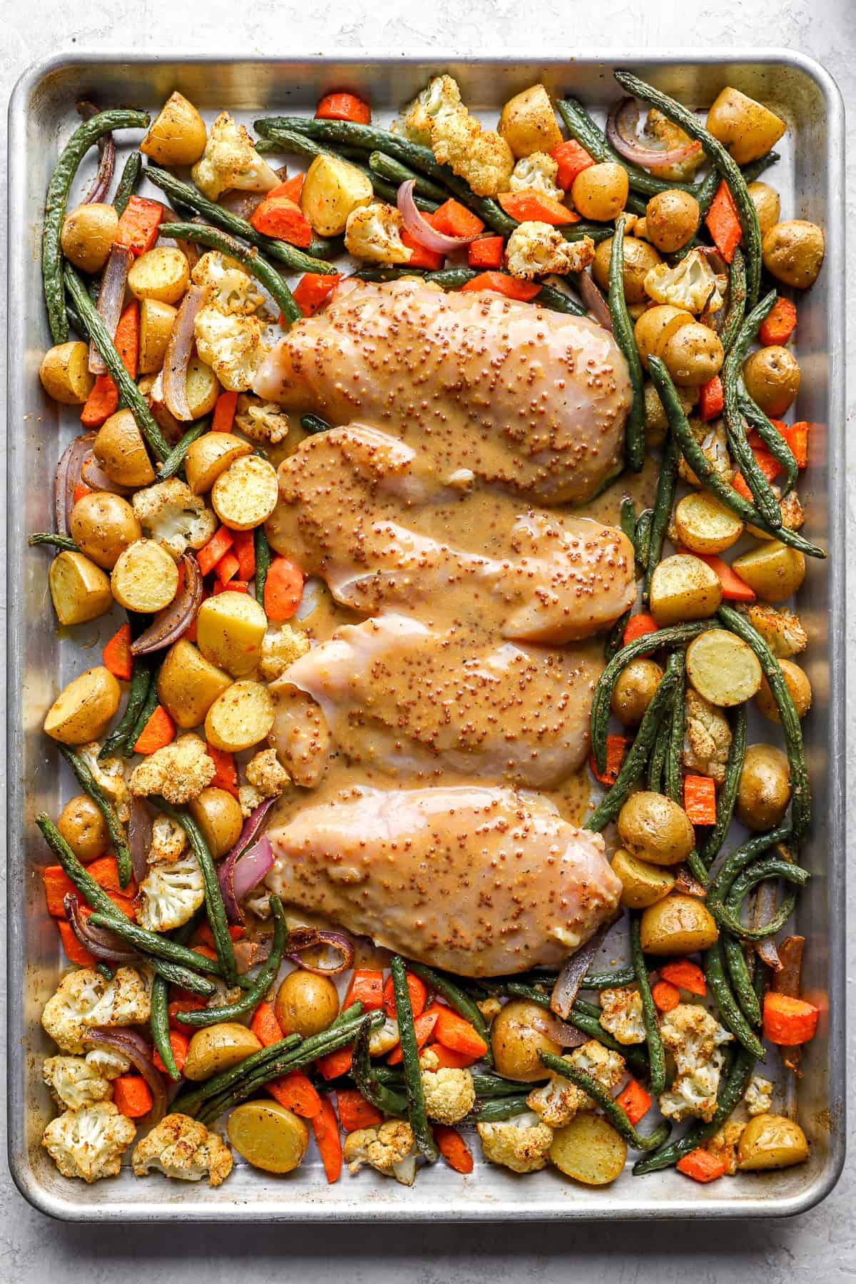 Raw honey mustard chicken on a sheet pan with vegetables.