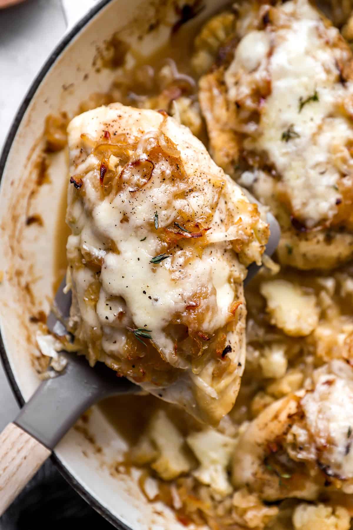 A piece of French onion baked chicken being lifted from a pot. 