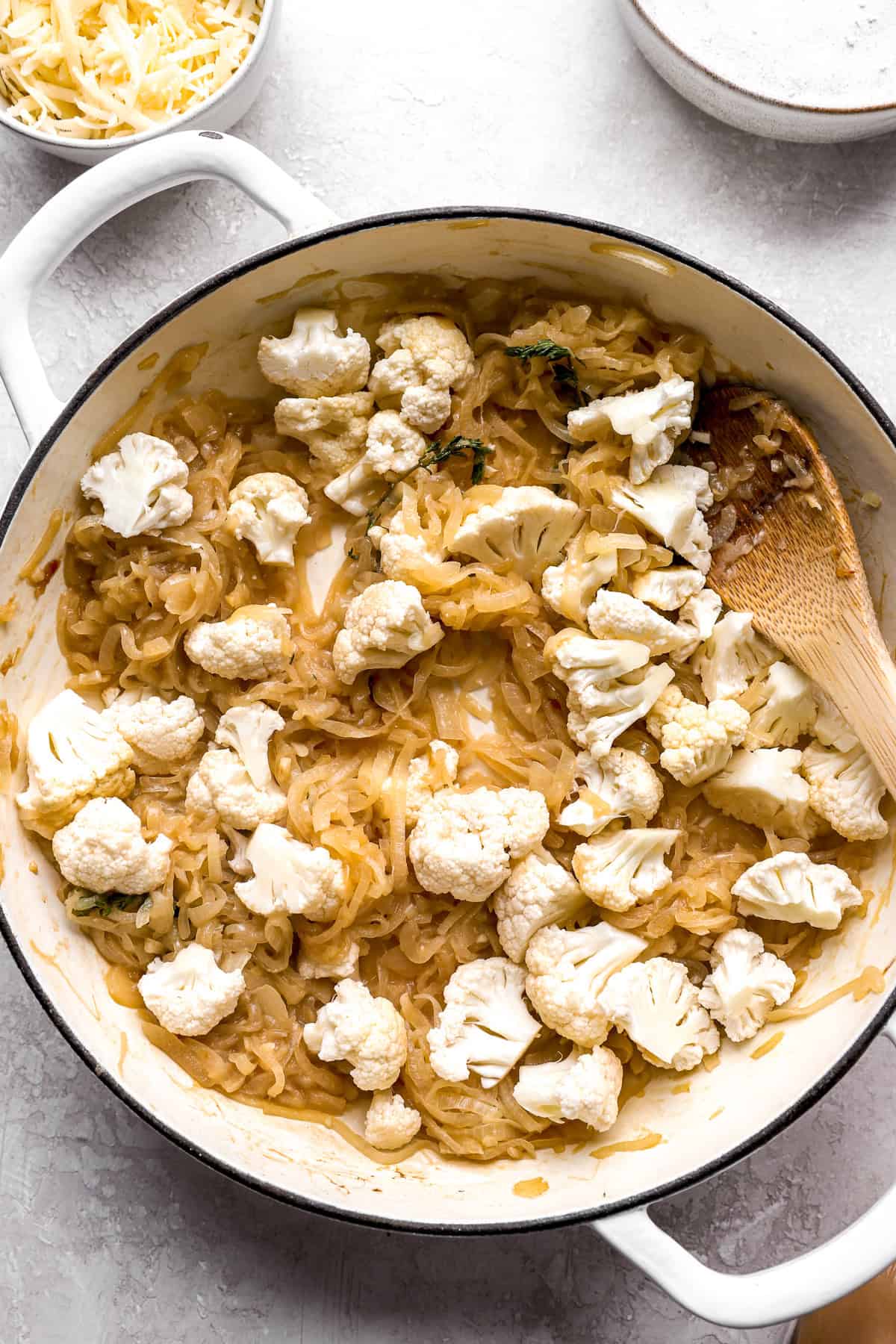 Cauliflower being added to caramelized onions in a skillet.