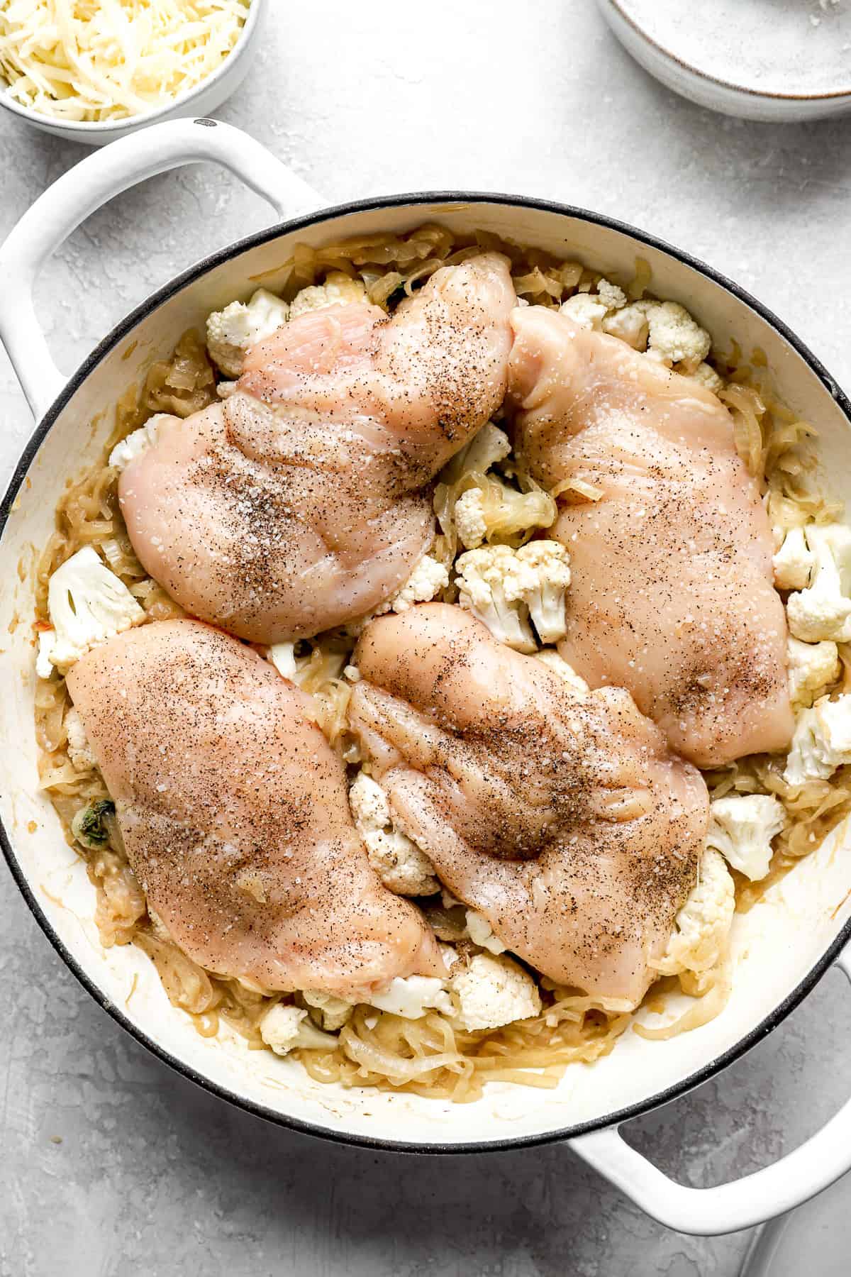 Raw chicken breasts on top of cauliflower and caramelized onions. 