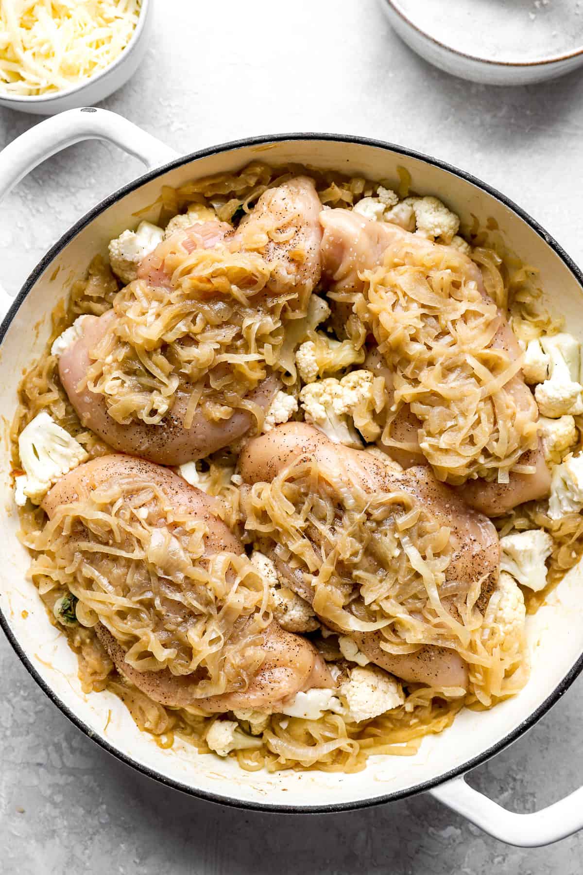 Caramelized onions on top of raw chicken in a skillet. 