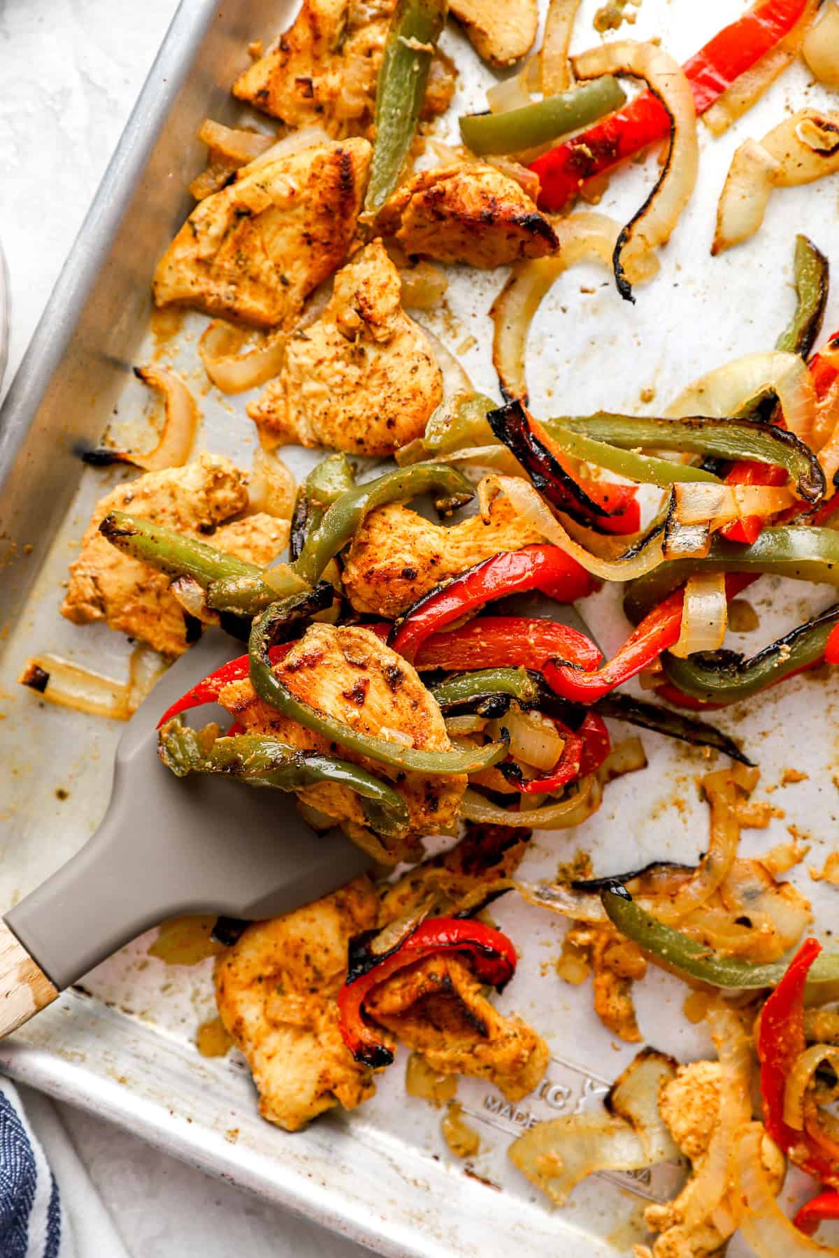 A spatula lifting a scoop of chicken fajitas from a pan. 