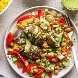 A plate of kofta meatballs with veggies, chickpeas, turmeric rice, and green tahini.