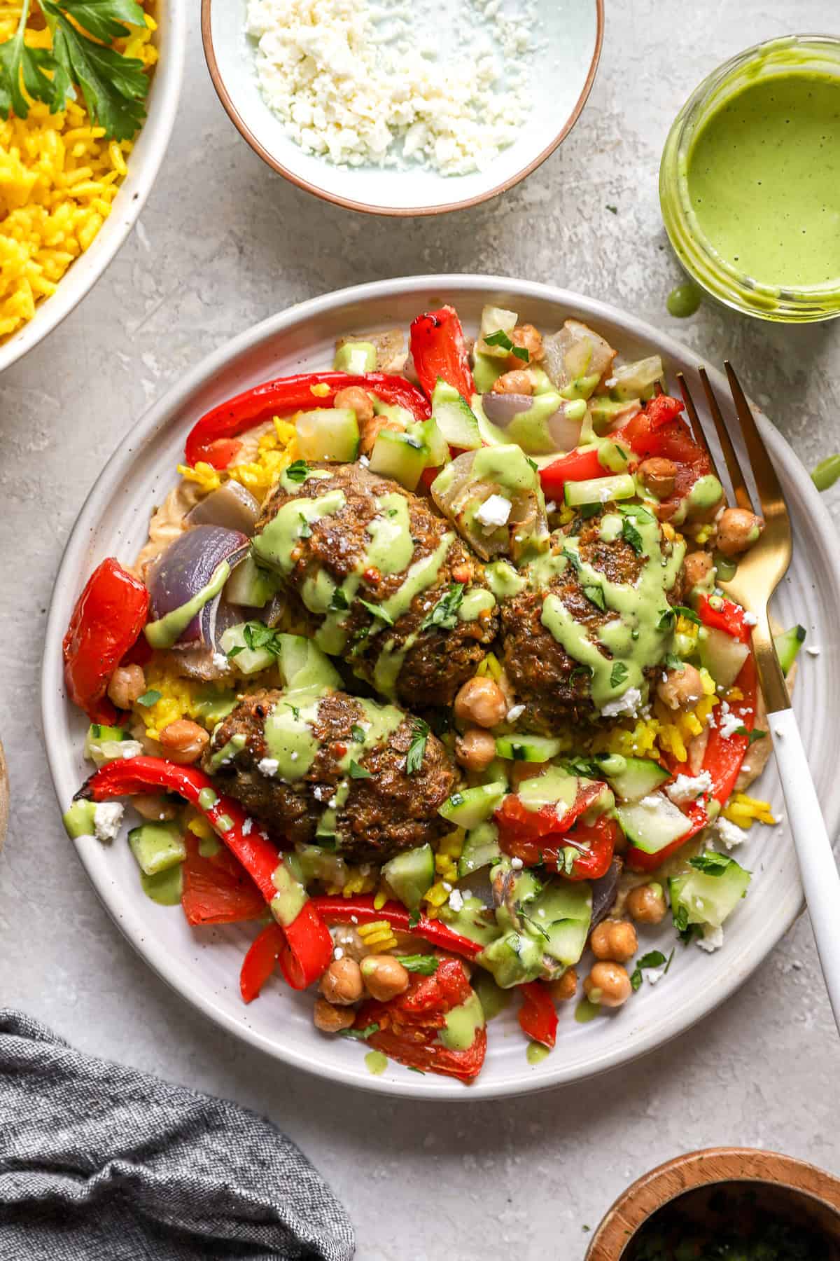 A plate of kofta meatballs with veggies, chickpeas, turmeric rice, and green tahini.