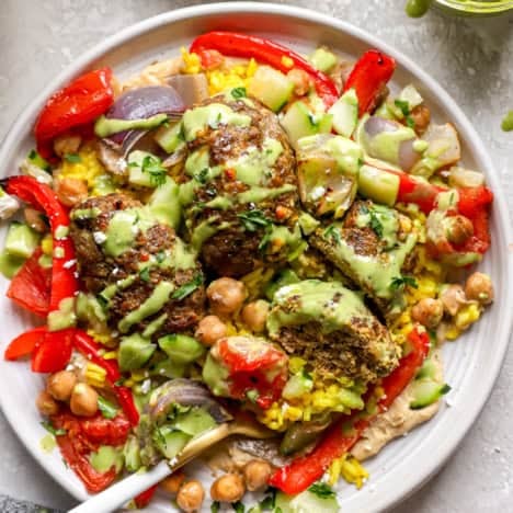 A fork on a plate with kofta meatballs, veggies, chickpeas, turmeric rice, and green tahini.