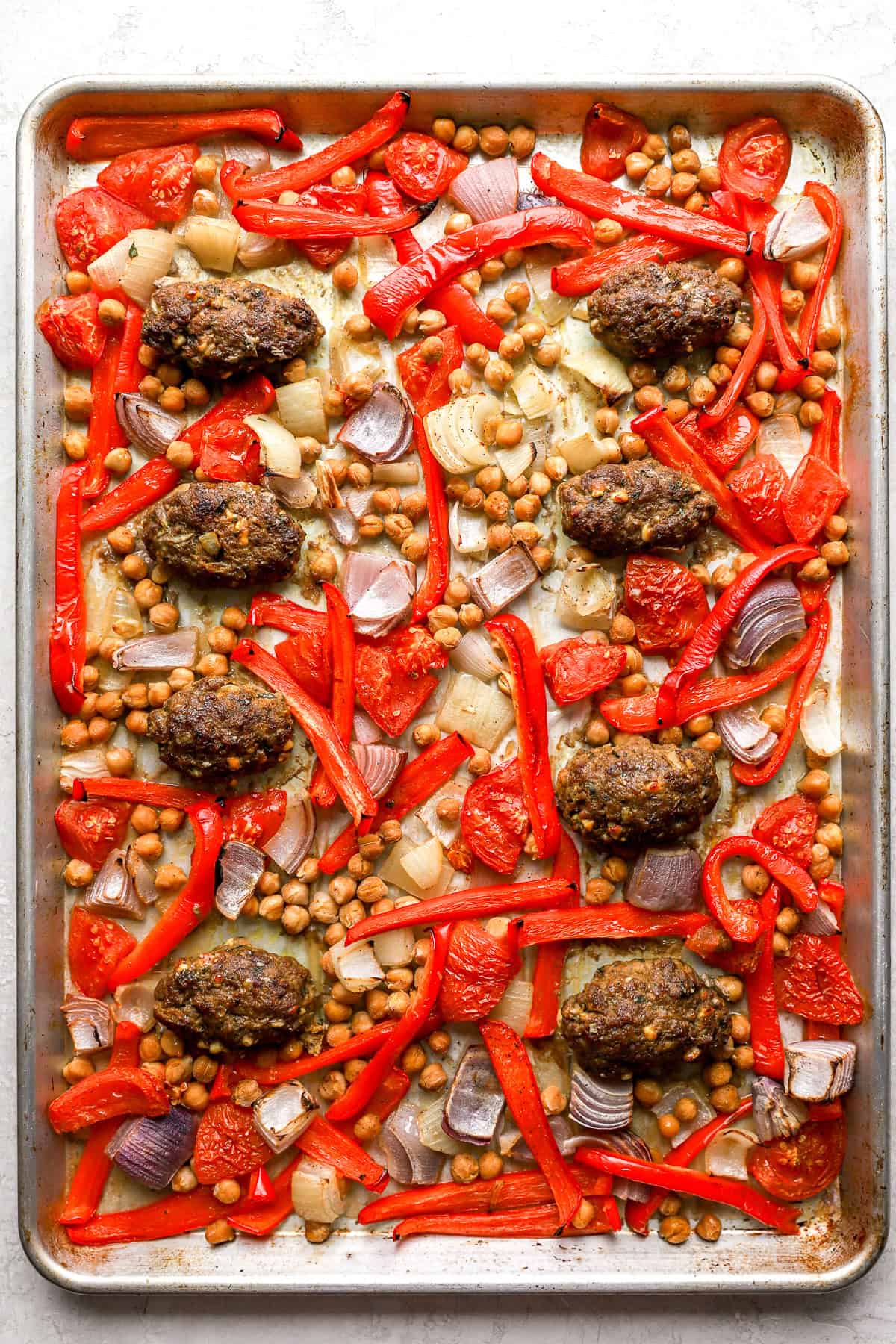 Baked kofta meatballs on a baking sheet with veggies and chickpeas.