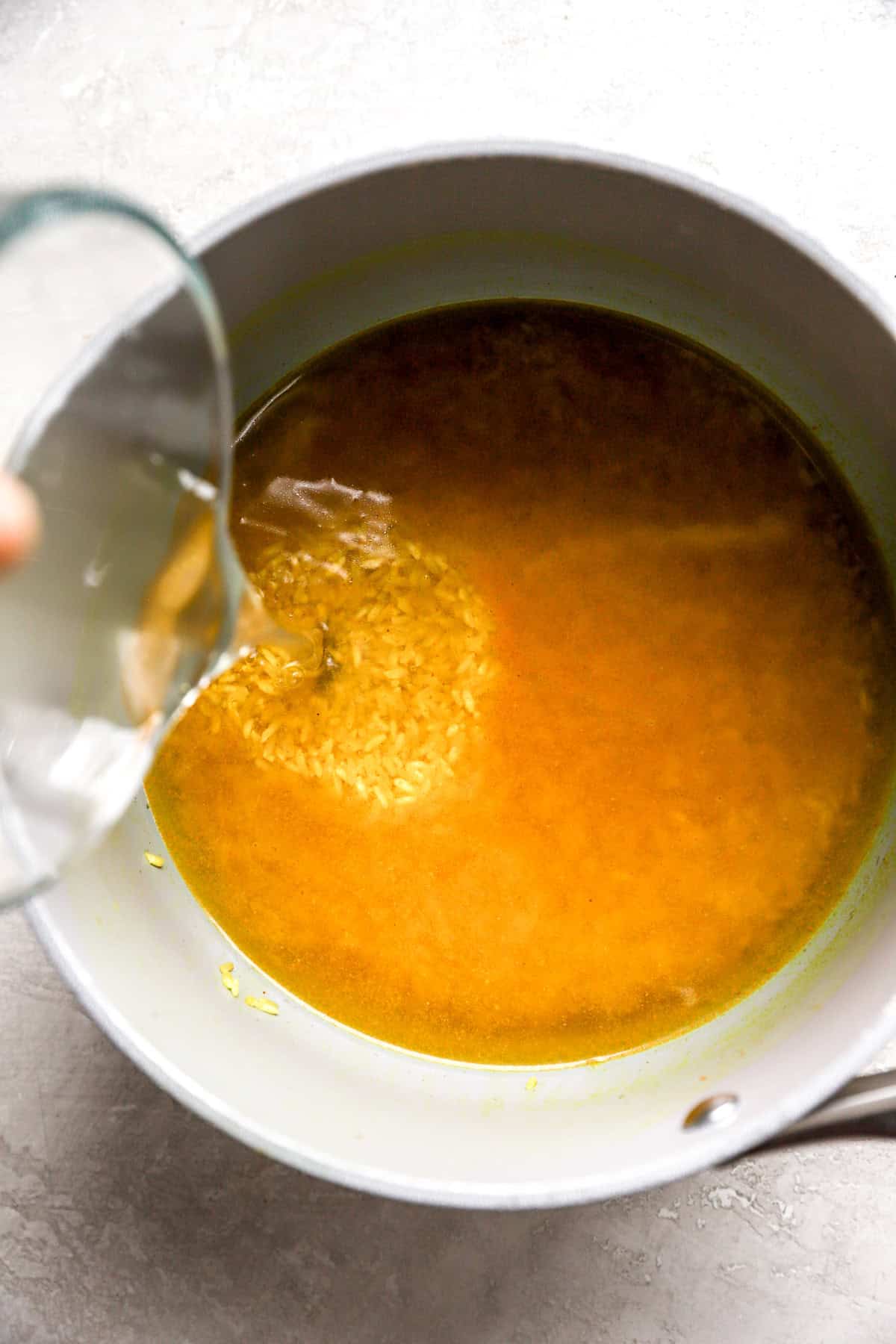 Broth being poured into a pot of turmeric rice. 