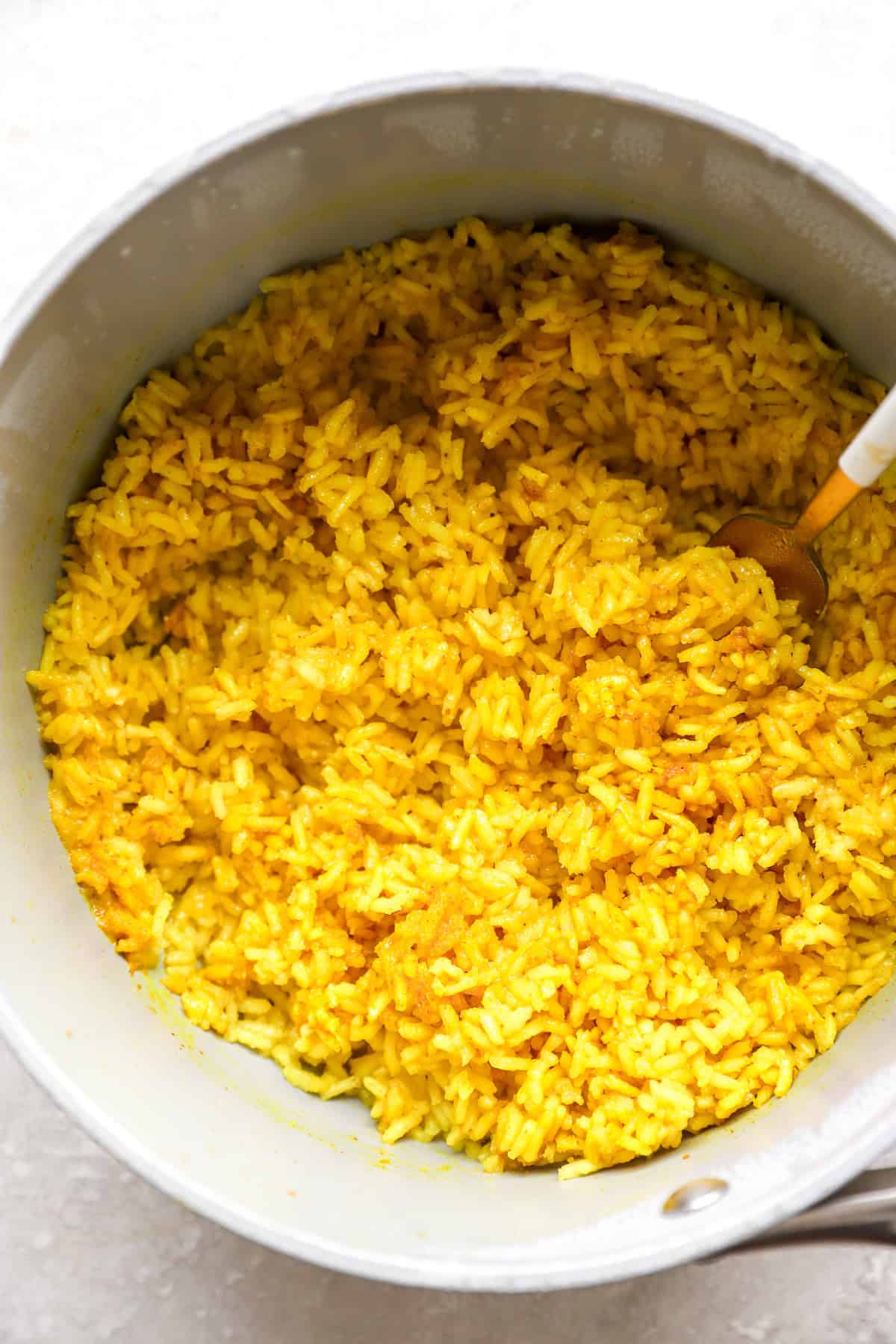 Cooked turmeric rice being fluffed in a pot. 