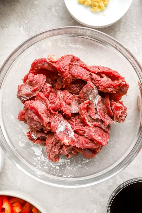 Raw beef strips in a bowl tossed with flour. 