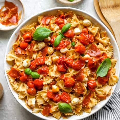 A bowl of caprese pasta salad topped with tomato confit and fresh basil.
