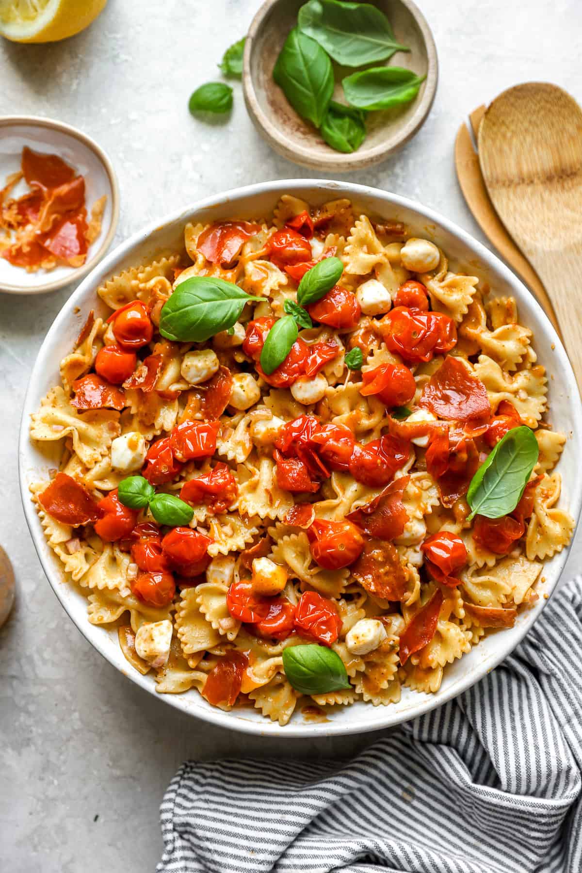 A bowl of caprese pasta salad topped with tomato confit and fresh basil.