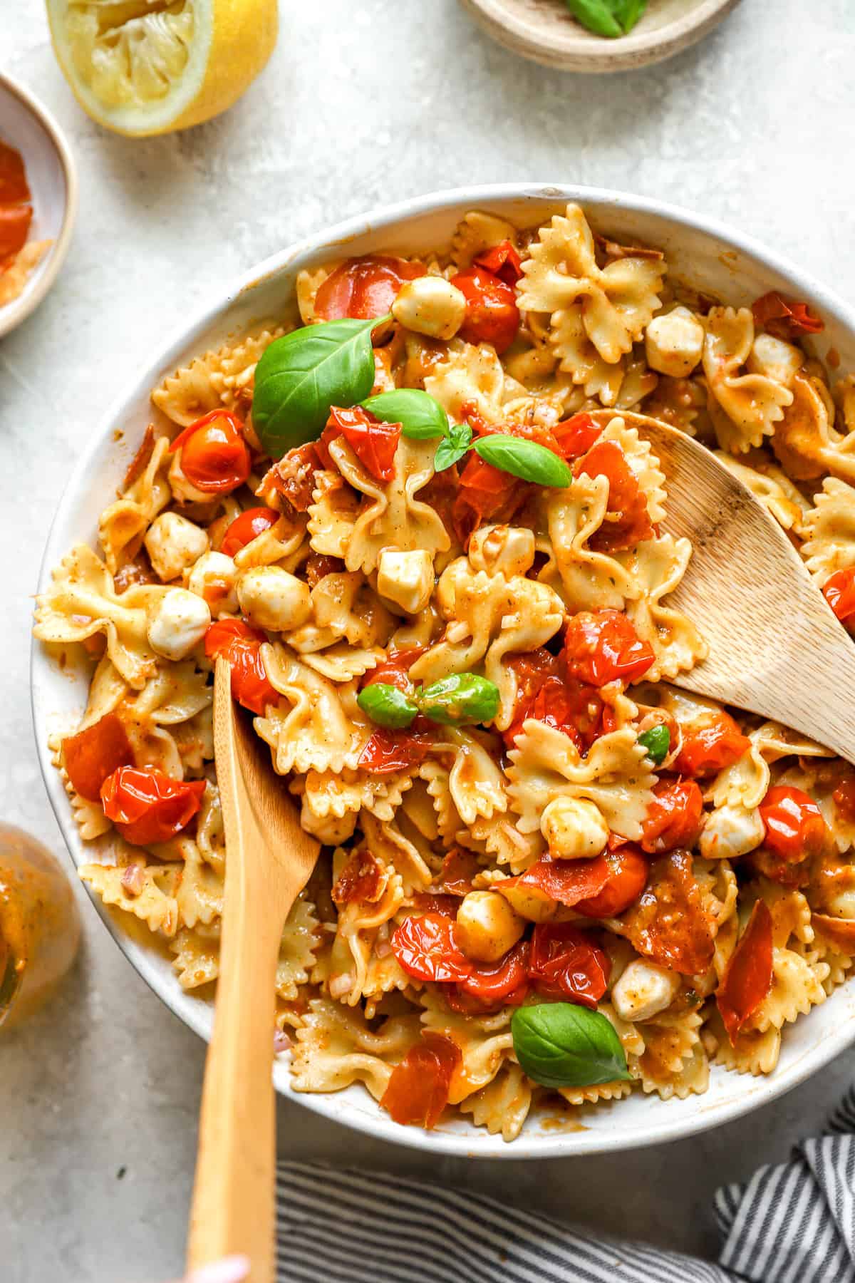 A caprese pasta salad being tossed in a bowl. 