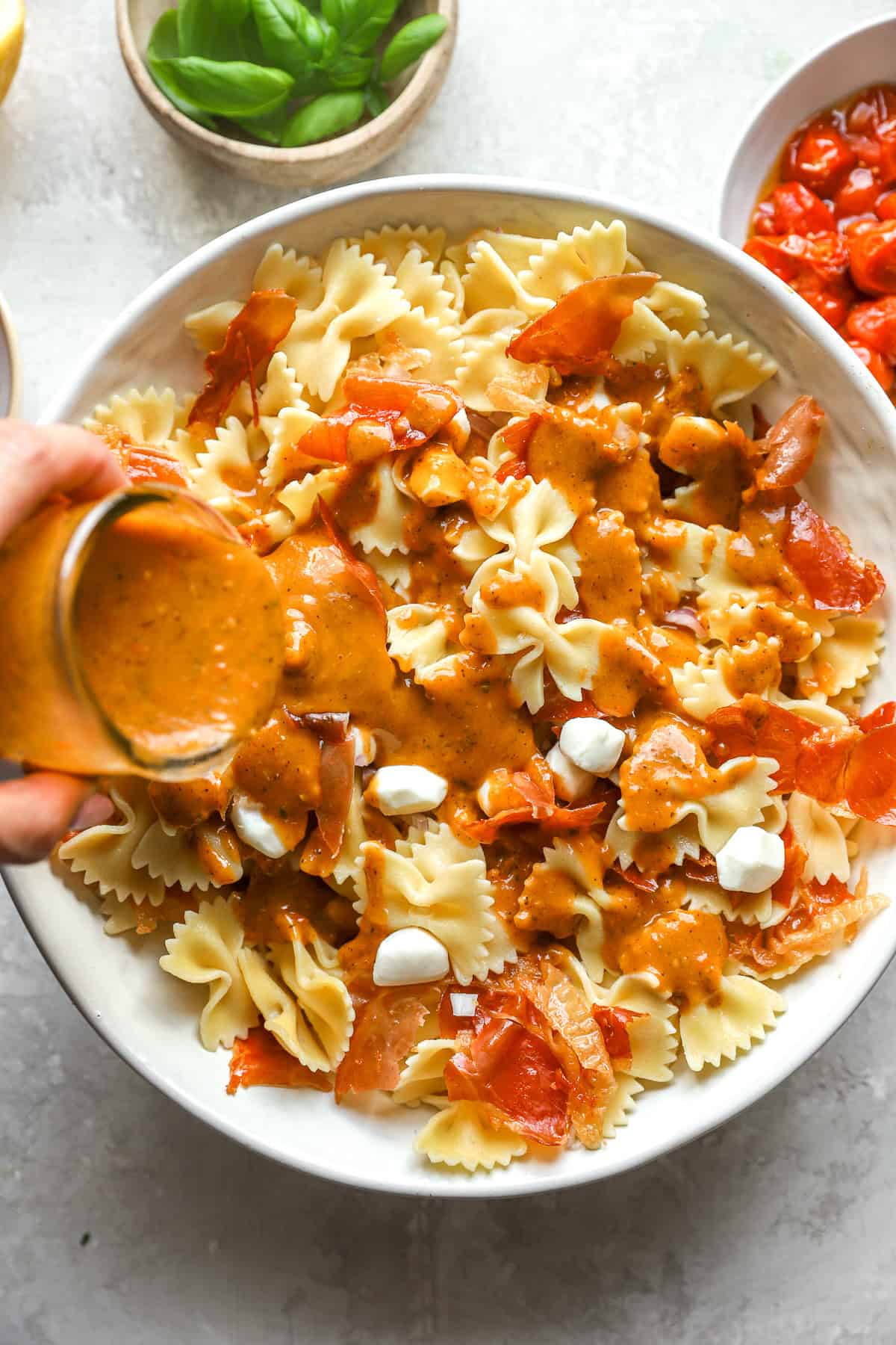 Tomato confit dressing being drizzled over a caprese pasta salad. 