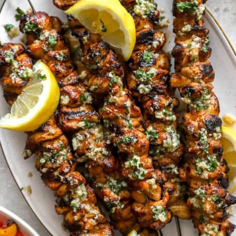 A platter of lemon pepper Parmesan chicken skewers with lemon wedges.