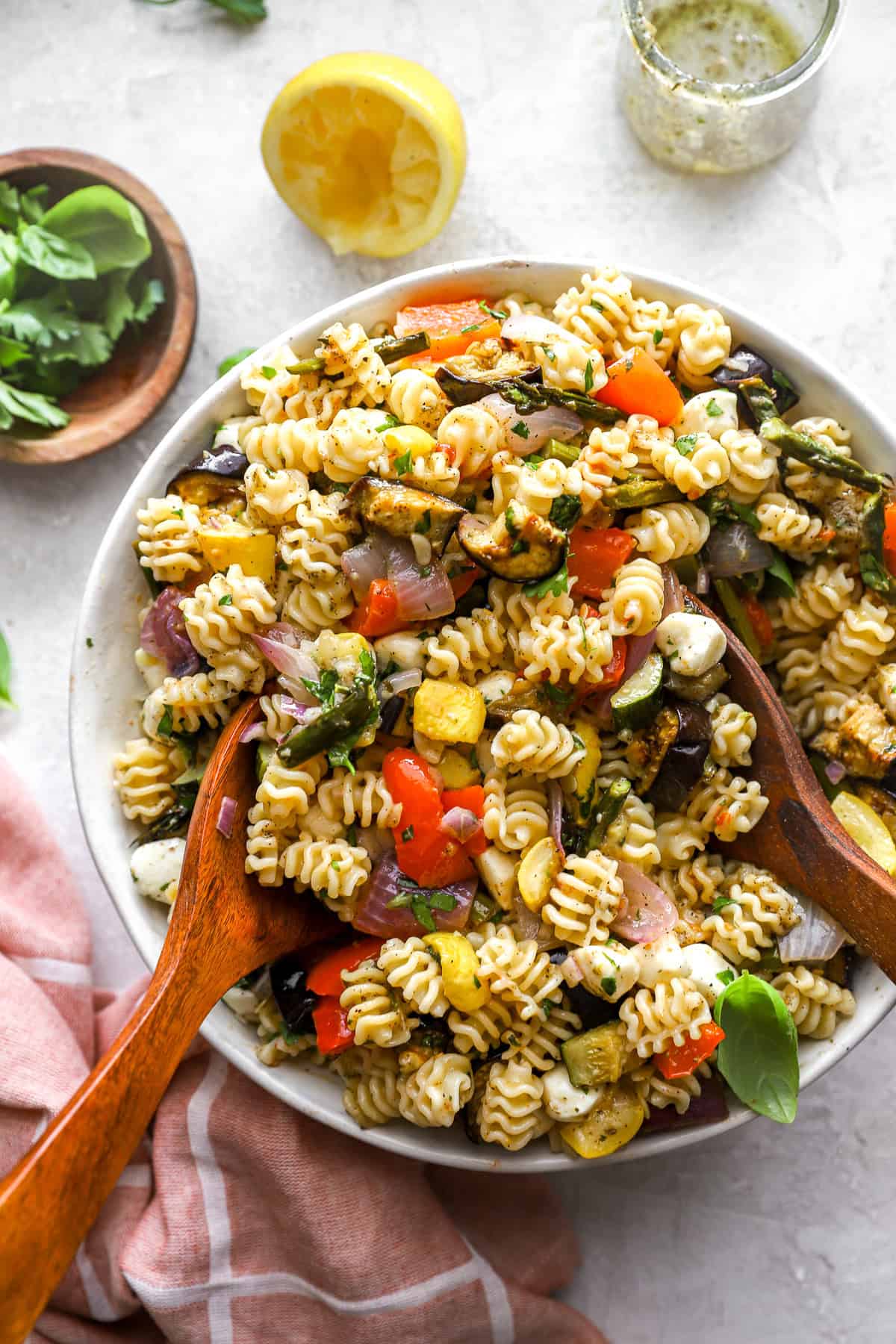 A Mediterranean pasta salad being tossed with wooden spoons.