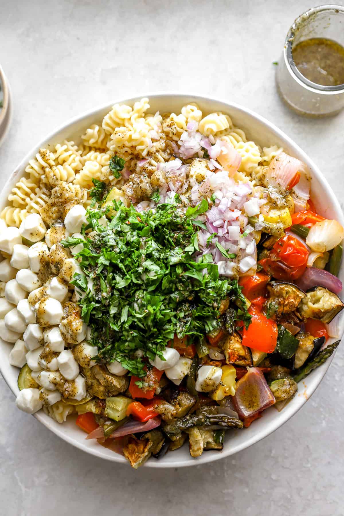 Pasta, roasted vegetables, fresh herbs, and mozzarella in a bowl.