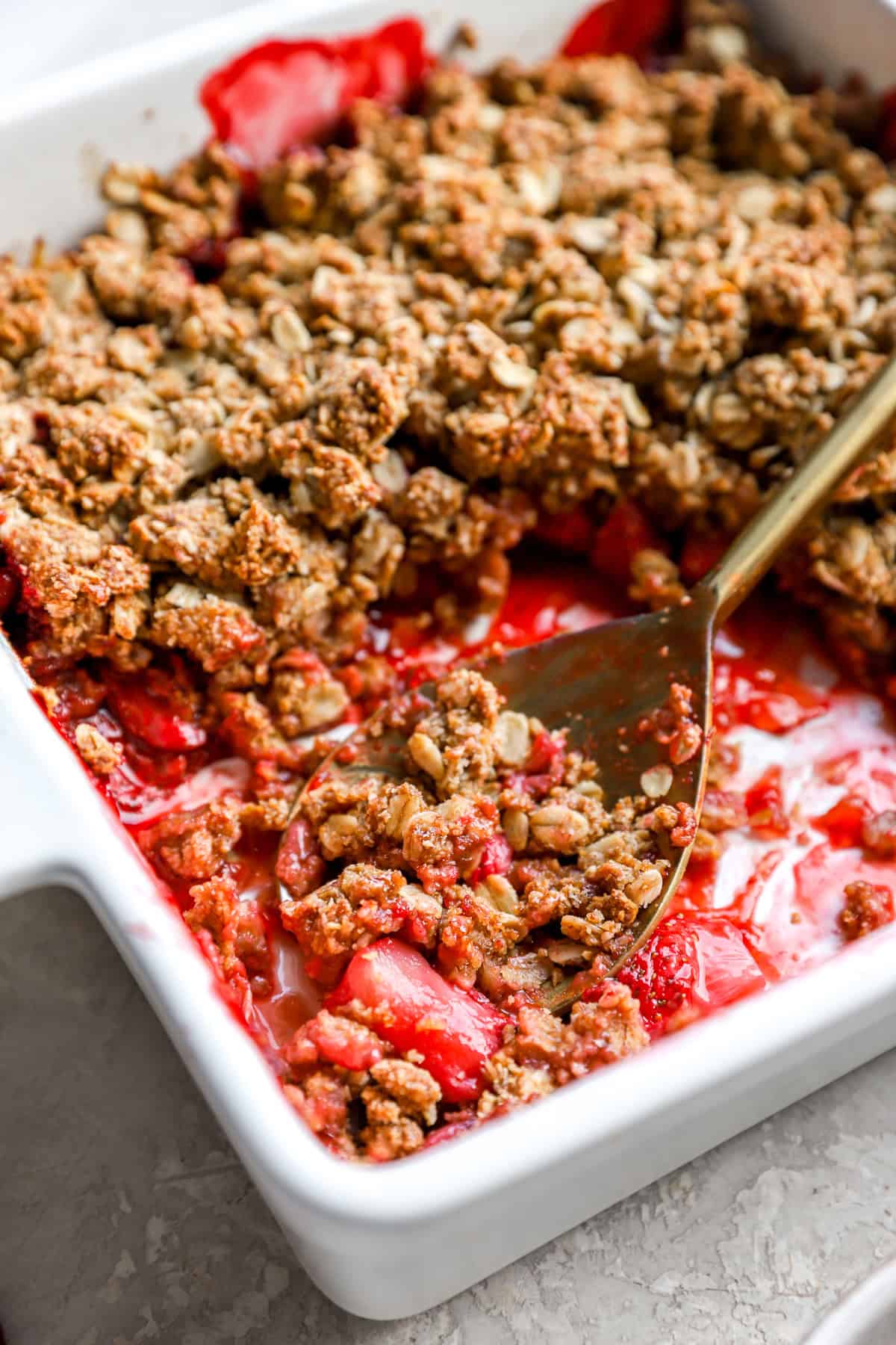 A spoon in a baking dish of gluten-free strawberry crisp.