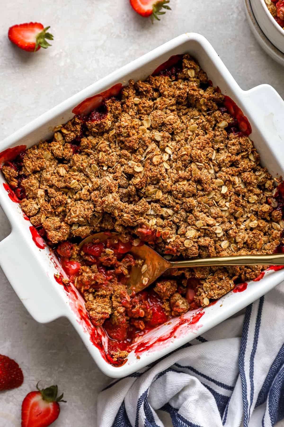 A square baking dish full of strawberry crisp with a portion missing. 