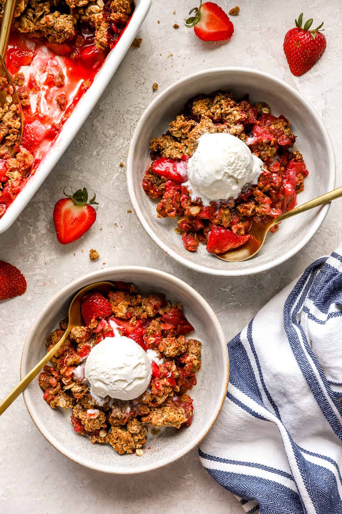 Two bowls of gluten-free strawberry crisp topped with vanilla ice cream.