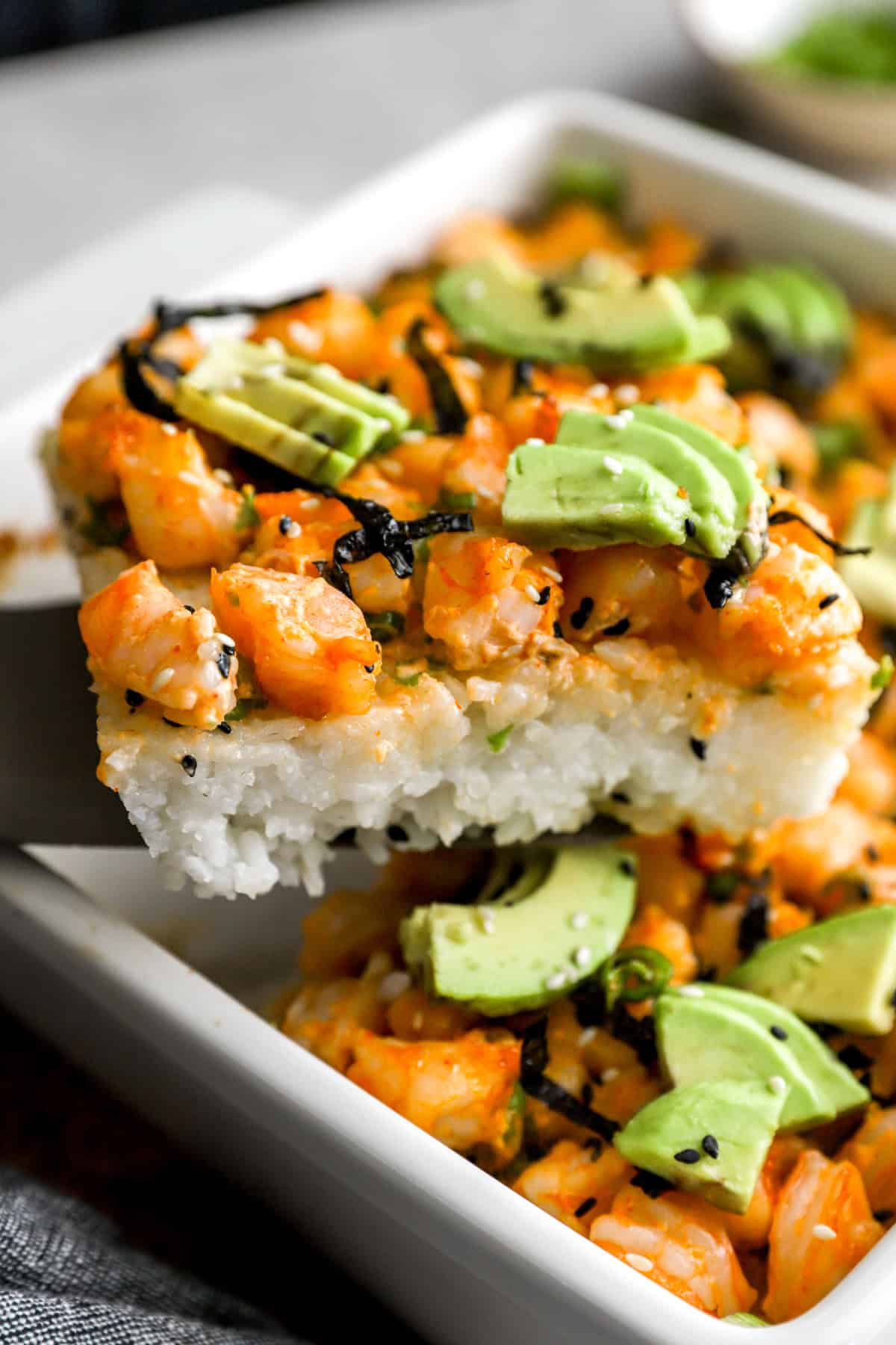 A slice of shrimp sushi bake being lifted from a baking dish.
