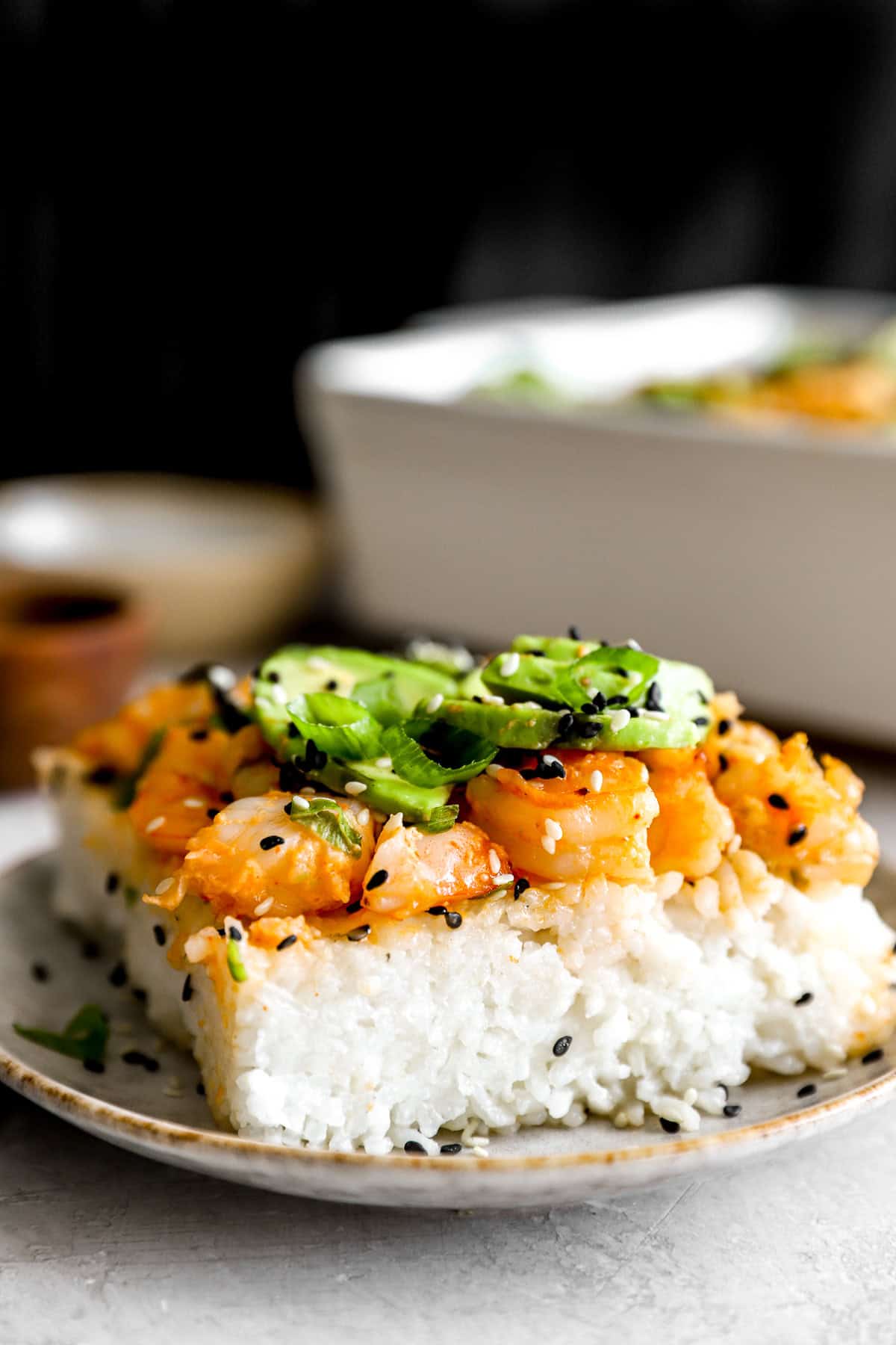 A slice of shrimp sushi bake topped with avocado on a plate. 