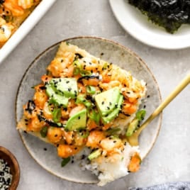 A slice of shrimp sushi bake on a plate with a fork holding a bite.