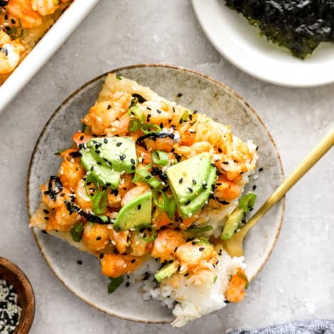 A slice of shrimp sushi bake on a plate with a fork holding a bite.