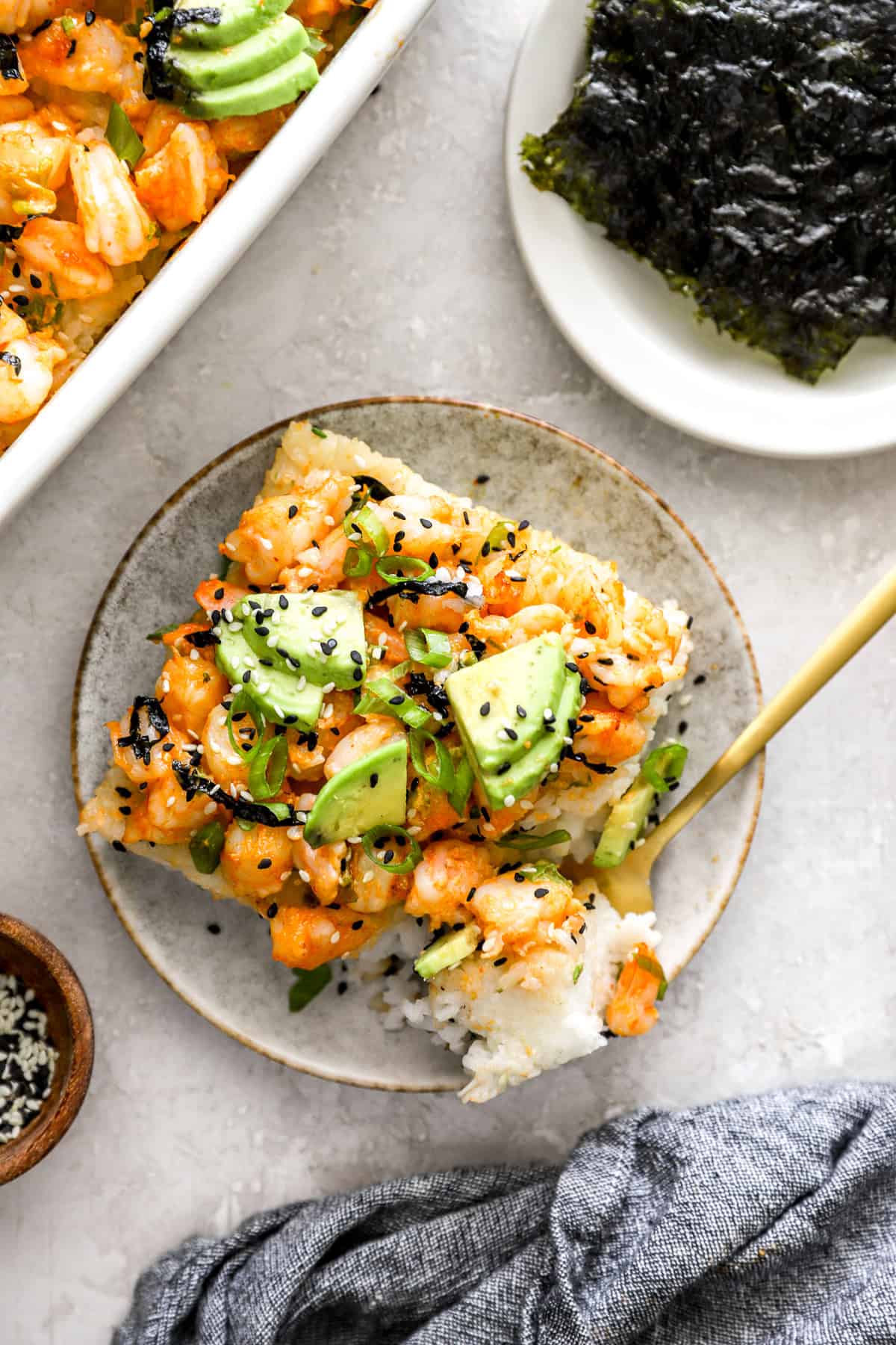 A slice of shrimp sushi bake on a plate with a fork holding a bite.