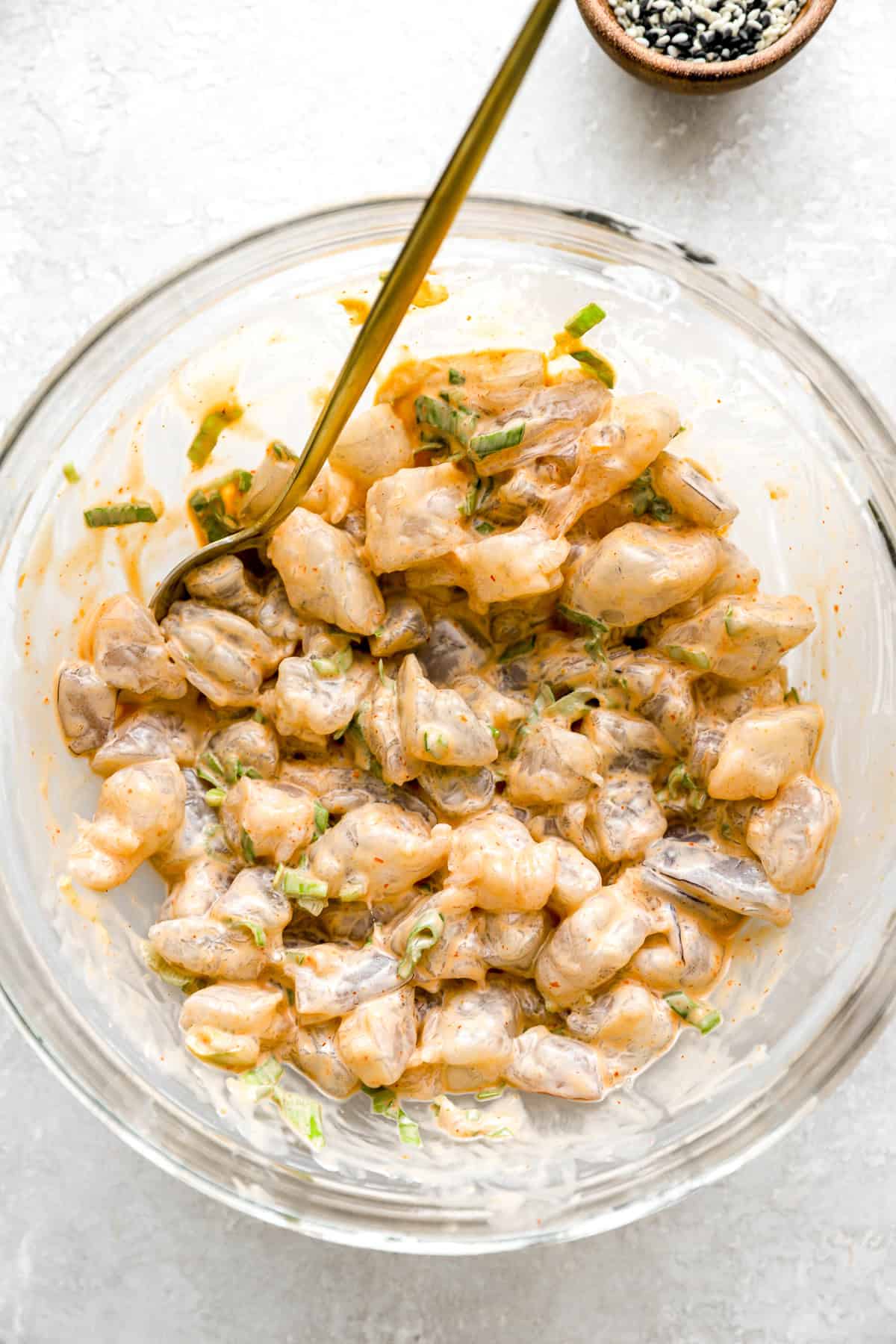 Raw shrimp being tossed in a bowl with spicy mayo. 