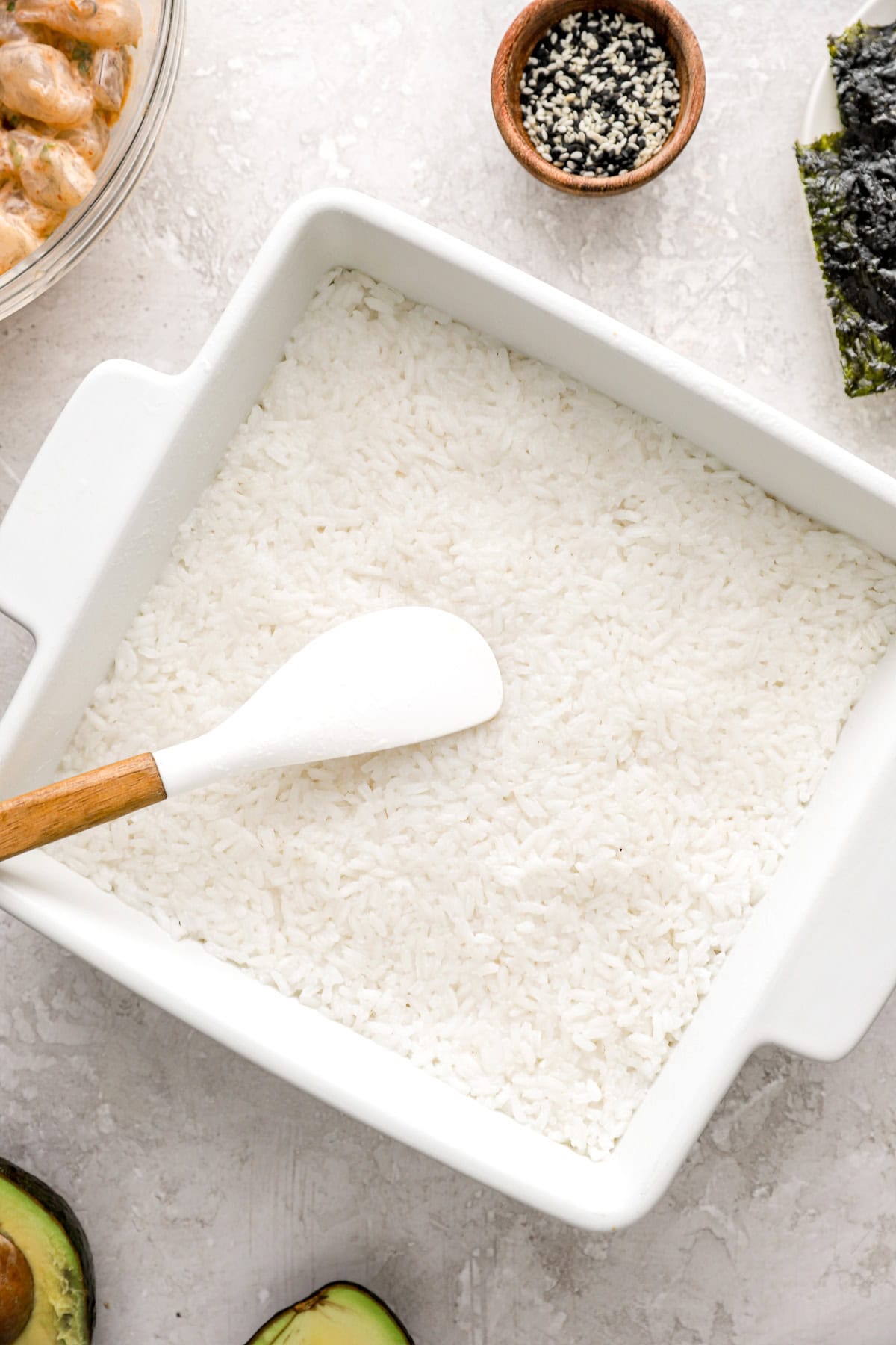 White rice being spread evenly in the bottom of a baking dish. 