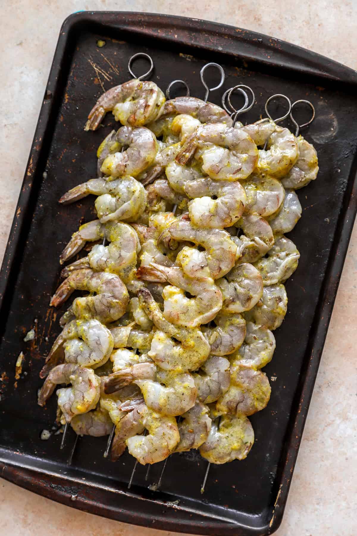 Raw marinaded shrimp on metal skewers.