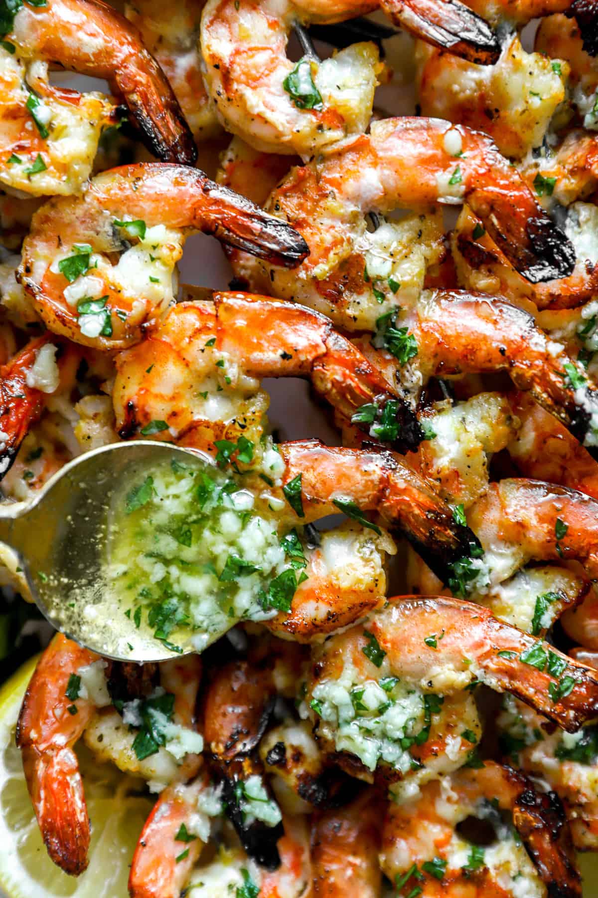 Garlic butter being spooned over grilled shrimp skewers. 