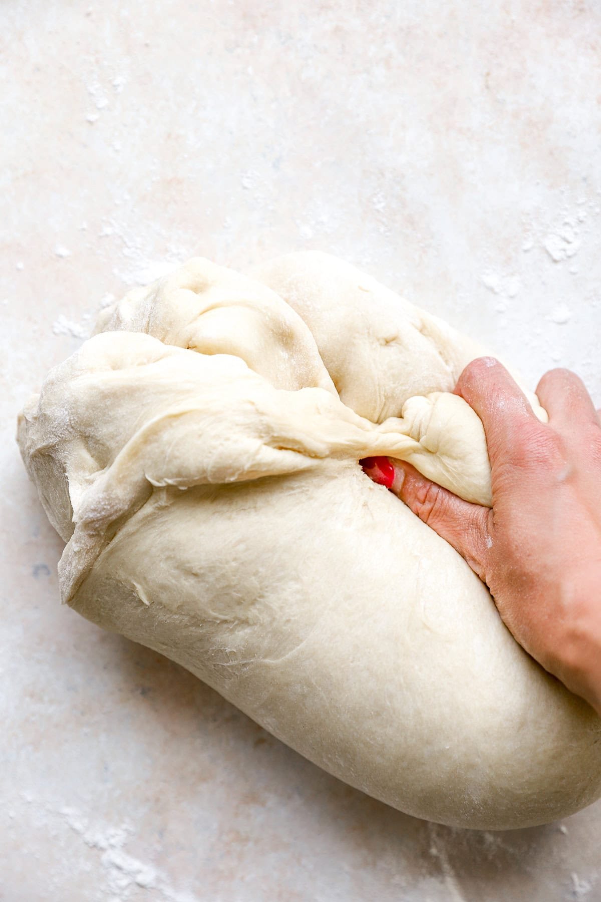 A hand punching down challah bread dough.