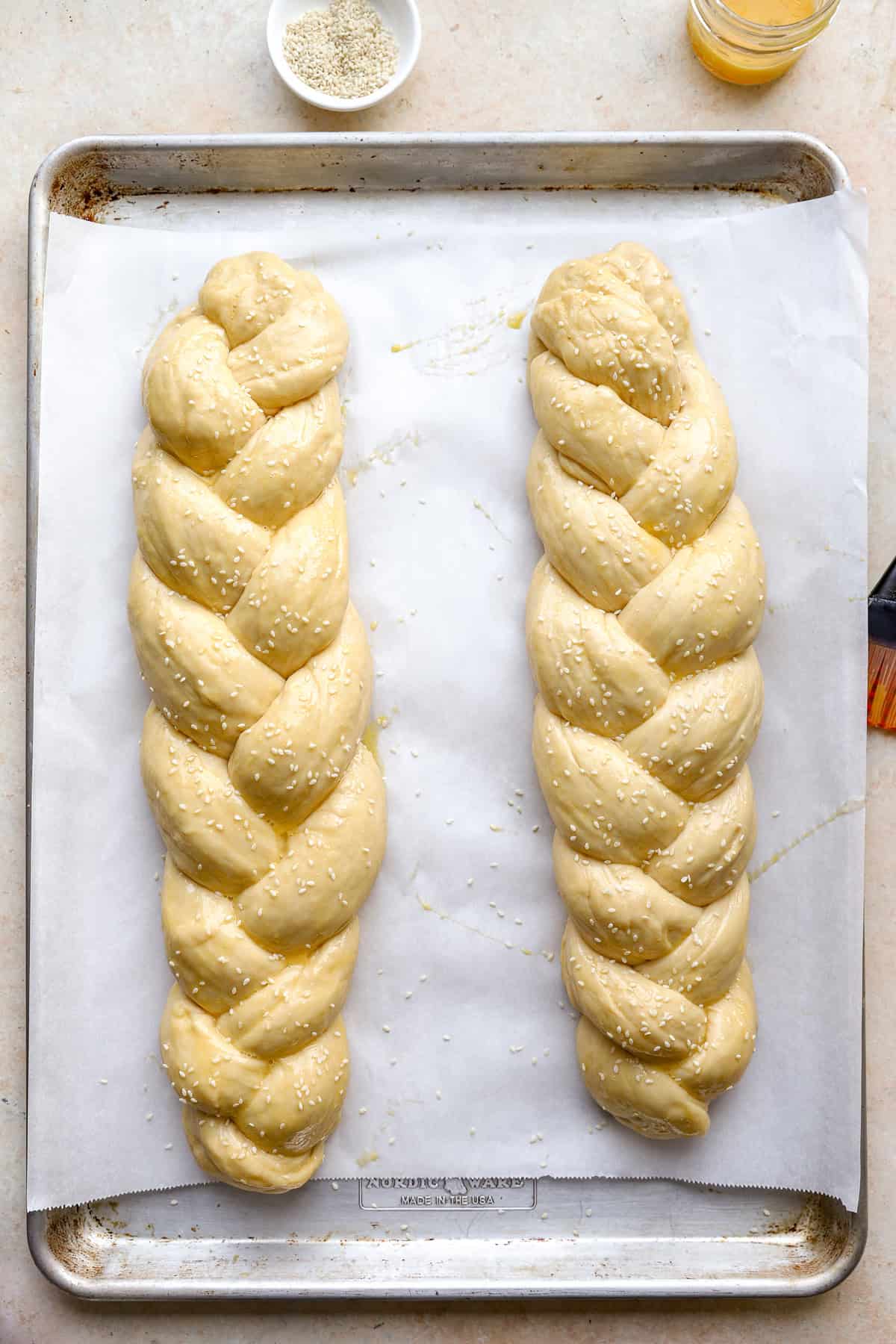 Two unbaked loaves of Challah bread on a parchment paper lined baking sheet.
