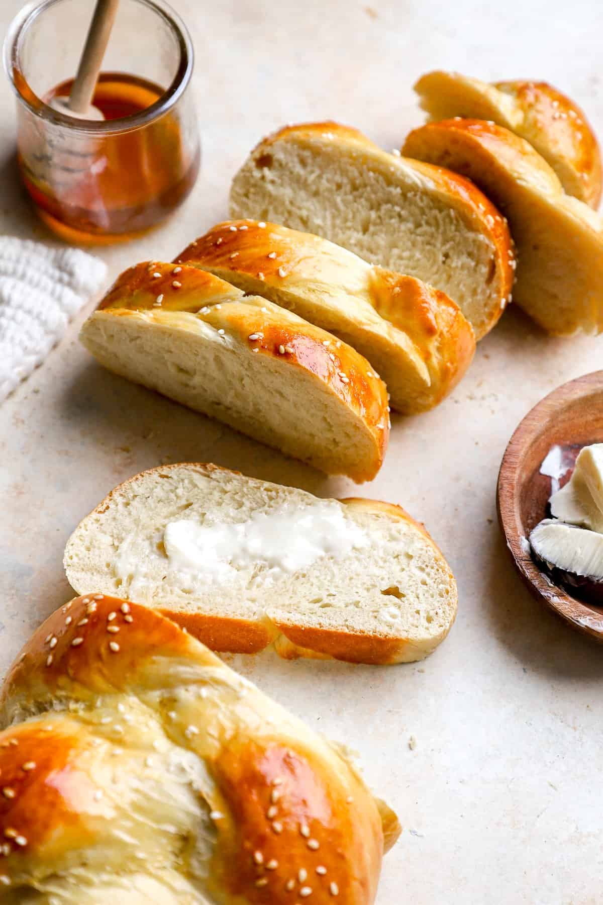A sliced loaf of Challah bread, one piece topped with butter.