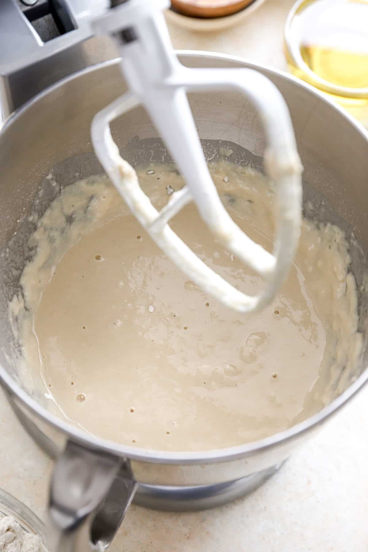 A yeast and flour mixture in a stand mixer fitted with a paddle attachment.
