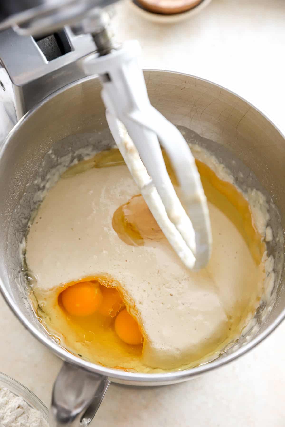 Wet ingredients being added to bread dough in a stand mixer.