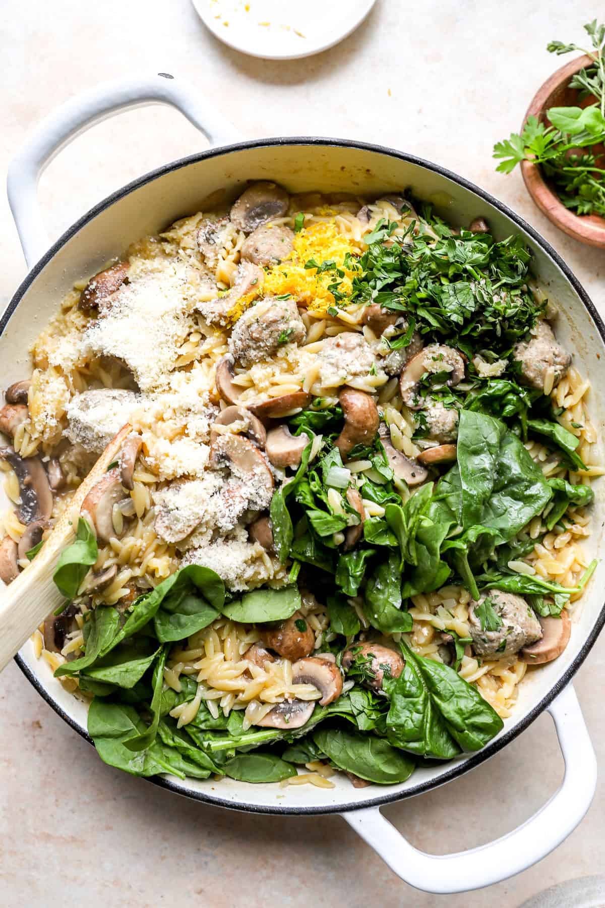 Parmesan cheese and spinach being stirred into a pot of meatballs with orzo.