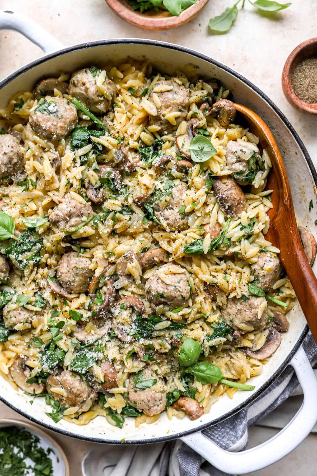 A pot of meatballs with orzo with a wooden spoon on the side.