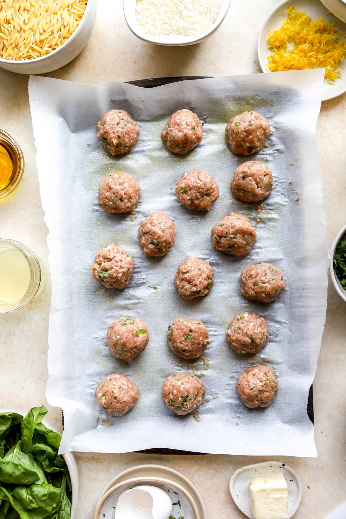 Raw meatballs on a parchment paper lined baking dish.