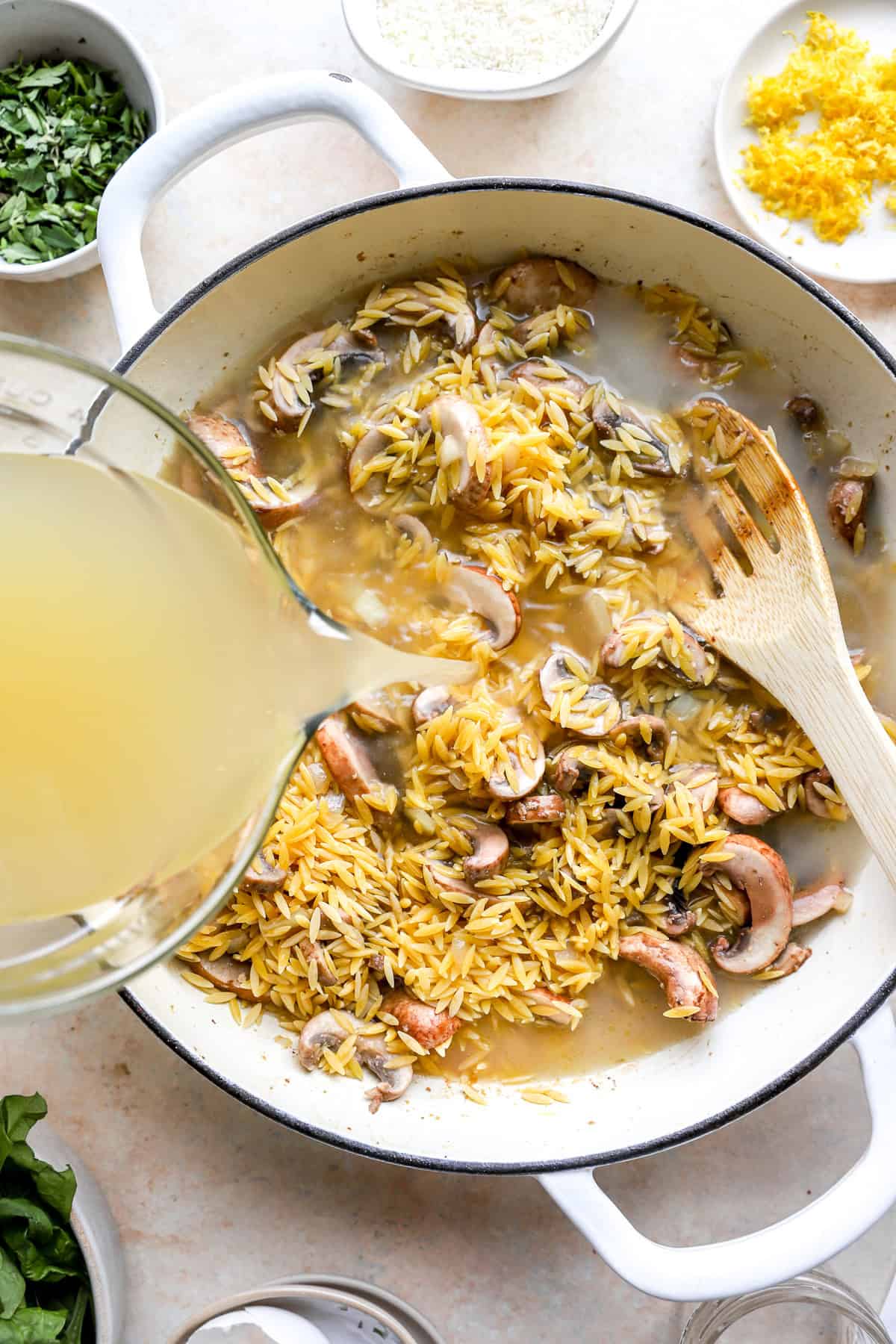 Broth being poured into a pot of mushrooms and orzo.