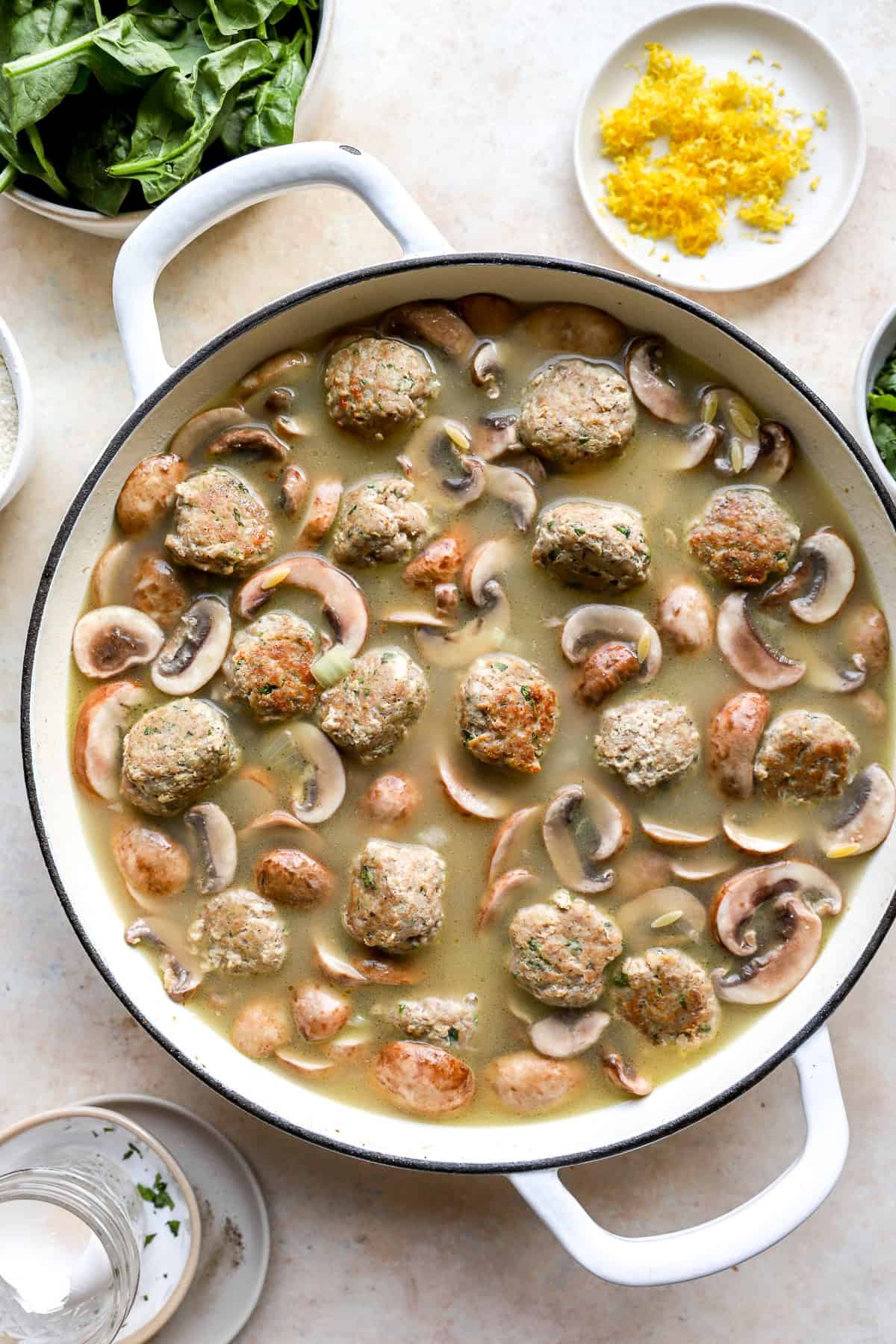 Meatballs, mushrooms, and orzo in a pot of broth.