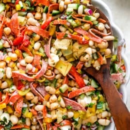A wooden spoon sticking out of a bowl of grinder bean salad.
