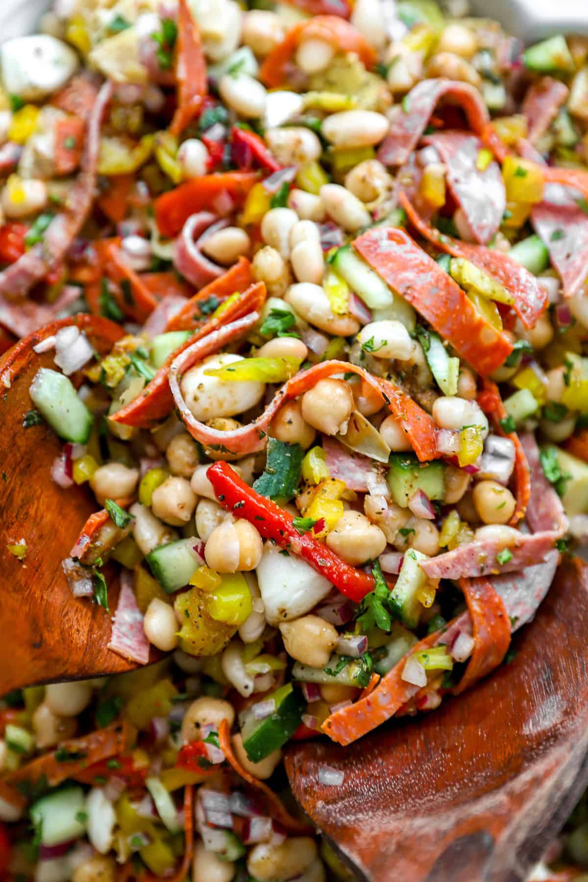 A wooden spoon lifting a scoop of grinder bean salad from a bowl. 