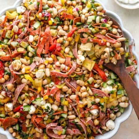A bowl of grinder bean salad with a wooden spoon sticking out.